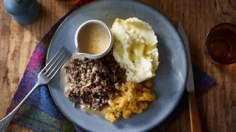 Haggis, neeps and tatties on a blue plate with a fork on the side