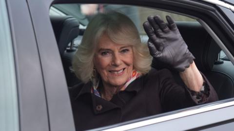 the Queen in a car waves through an open window, whilst wearing gloves