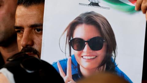  Photo of Aysenur Ezgi Eygi wearing sunglasses and blue shirt on a poster held by man with a mustache