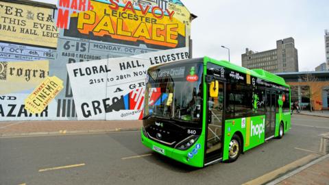 A small green bus in front of a colourful mural