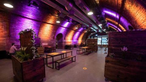 The inside of a bar and events space, with various tables and chairs set up, with the ceiling forming an arch over them 