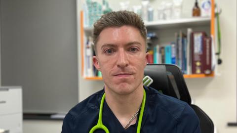 A doctor sat at his desk smiling at the camera.