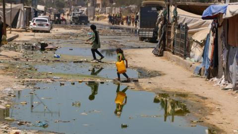 Children line up with bottles to get clean water on streets flooded with leaked sewage