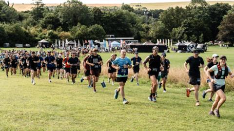 Dozens of people in running gear running across a field from left to right
