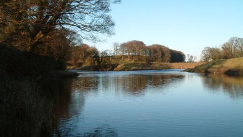 Sunset over the River Hodder surrounded by green and brown banks and trees
