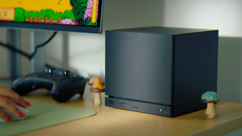 A large black cube sits on a desk. It has a strip cut out near the bottom, below which is a power button and three USB ports.