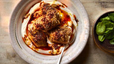 A large round deep platter of spiced chicken on a bed of yoghurt next to a small bowl of greens