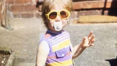 Nicola Williams aged three posing in shorts, sunglasses and wellington boots.