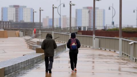 People walk along the sea front near to Old Portsmouth in Hampshire in the rain.