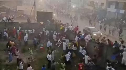 A screengrab showing many people scrambling to get out of a football field in Guinea, some climbing onto a wall