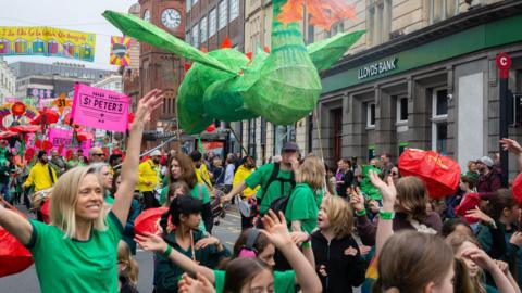 A colourful parade through the streets of Brighton with a paper dragon being held in the air