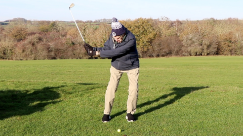 Archie Hemsley is pictured mid golf swing. He is wearing beige trousers, a navy fleece and a bobble hat