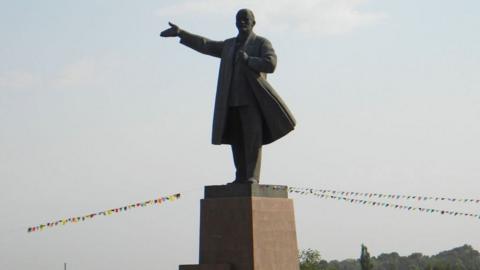 The statue of Vladimir Lenin, stood with an arm extended, against a grey sky in Osh Kyrgyzstan