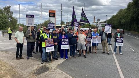 A group of national coal mining museum staff on a picket line. They raise flags and placard. 