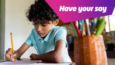 A young boy sits on a table at home writing