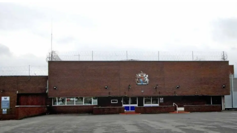 A largely brown building is in the bottom half of the image. A fence is seen above it in the photo, which was taken outside.