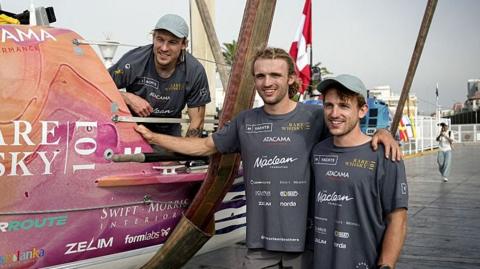 The three Maclean brothers next to their boat at Callao port in Peru before sailing across the Pacific. Two of the brothers are stood next to the boat and the other is in the boat