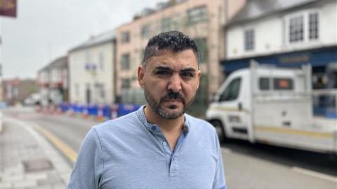 A business owner standing in front of the scaffolding which is three storeys tall.