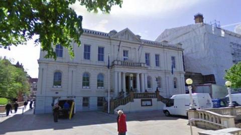 A white building with steps leading to the main entrance, which has a number of columns.