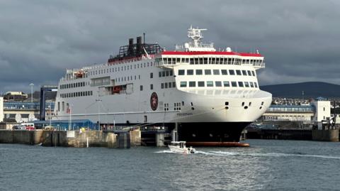 The Manxman ferry moored in Douglas Harbour. It is in the Steam Packet colours of red white and black and has the company's logo of a three-legs-of-Mann on this side.
