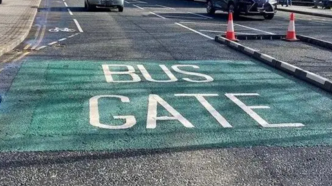 A sign of a busy road in Sheffield, with a green painted square on the floor with the words Bus gate.