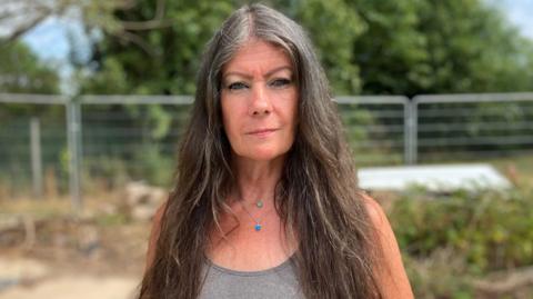 Woman with a grey top and long dark hair stood in front of an empty space