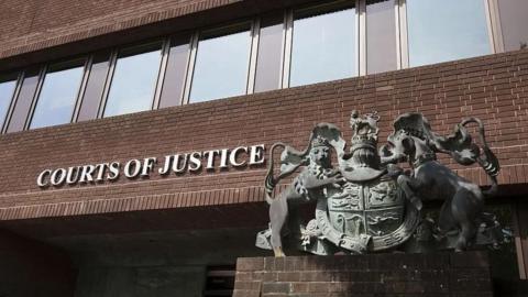 The exterior of Portsmouth Crown Court - a brown brick building with the words 'Courts of Justice' and a metal sculpture of the royal crest