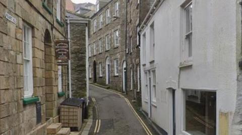 Google Street View image of Polkirt Hill in Mevagissey. It is a narrow single-lane road with double yellow lines on either side. Buildings line the road on both sides.