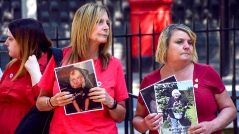 Family members of people who died from coronavirus hold pictures of their loved ones during a demonstration outside the UK Covid-19 Inquiry Hearing Centre in west London