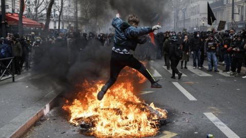 A protester jumps over burning debris in Paris