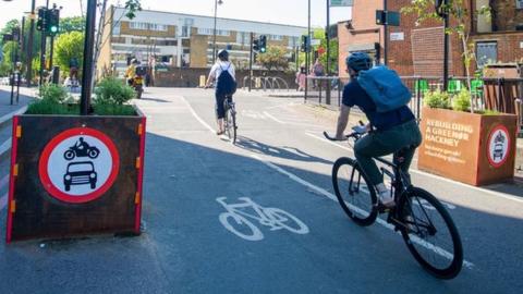 Cyclists ride through barriers marking an LTN on Middleton Road in the borough of Hackney.