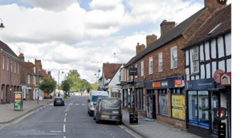 Stevenage High Street. There are shops on both sides and cars parked on the right side of the pavement