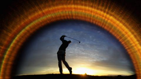 A golfer hits a ball into a setting sunset