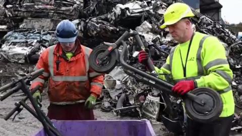 Two men in high viz load e-scooters into a purple crate