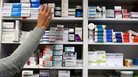 A pharmacist reaches for medication on a shelf