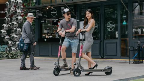 Two people on scooters in front of a cafe