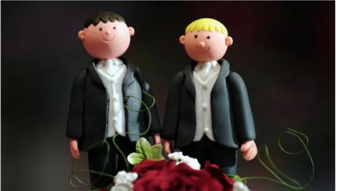 A wedding cake topper featuring two men