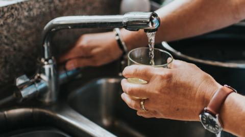 A person pours a glass of water from a tap