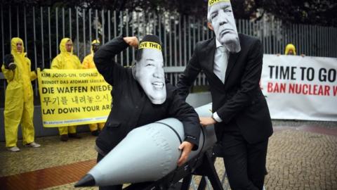 Activists dressed as Donald Trump and Kim Jong Un, tussle over a nuclear bomb in ican protest