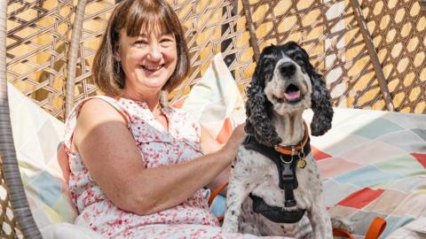 Carmel sat on a garden chair with a black and white spaniel.