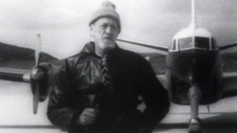 Black and white photo of a man standing in front of a plane