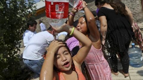 Two girls play refresh themselves while residents gather water from a fire hydrant at a neighborhood in Santiago, Chile, Monday, Feb. 27, 2017