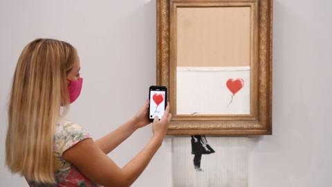 A gallery employee poses for photographers next to a painting entitled "Love is in the Bin" by anonymous British street artist Banksy at Sotheby"s auction house in London, Britain 03 September 2021.