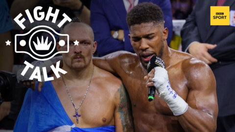 Anthony Joshua speaks on the mic with his arm around Oleksandr Usyk