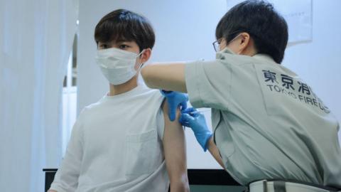 A Tokyo fire brigade staff member (R) administers a dose of the Covid-19 coronavirus vaccine at Aoyama University in Tokyo on August 2, 2021.