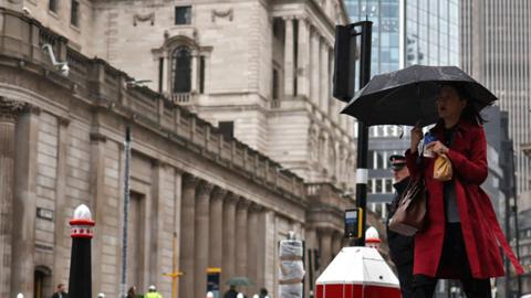 A pedestrian with an umbrella walks by the Bank of England building and Stock Exchange building, in the financial district, central London, on 2 November 2023