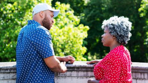 A man and woman stand outside having a conversation