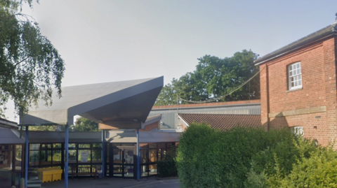 A view of the main entrance of the Dorking Community Hospital, a red brick and grey concrete and glass modern building.