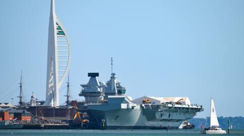 The Royal Navy's HMS Queen Elizabeth aircraft carrier with Portsmouth's Spinnaker Tower in the background, and a small yacht passing in the foreground