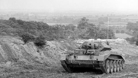 A World War Two tank drives over broken muddy ground